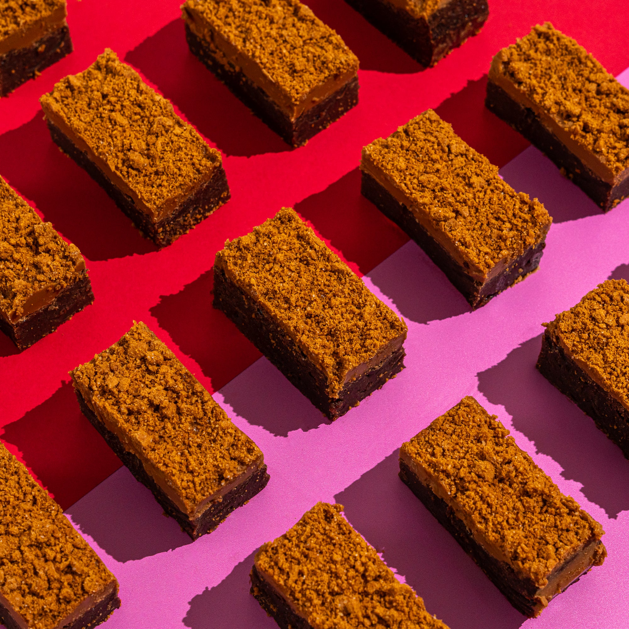 Biscoff topped fudgy soft brownies on a background of red and lilac