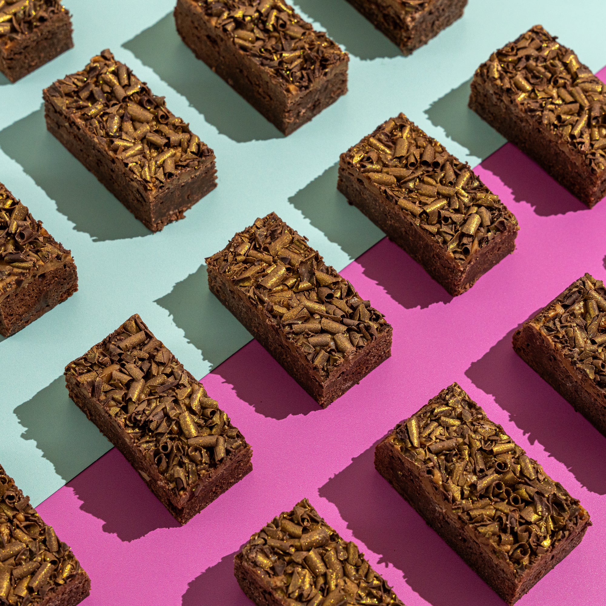 Fudgy salted caramel brownies topped with gold chocolate curls on an aqua and lilac background