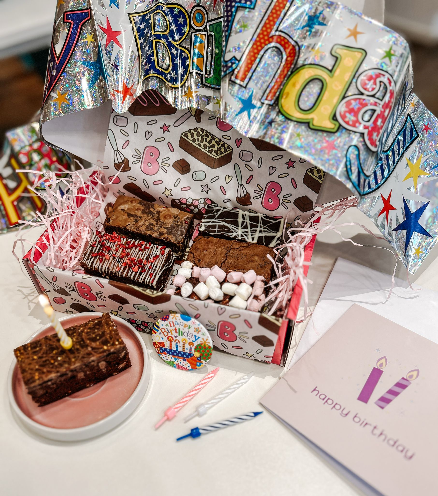 Birthday box celebration, with a birthday card, banner, badge and brownie with a candle in it as well as a gift box of brownies.